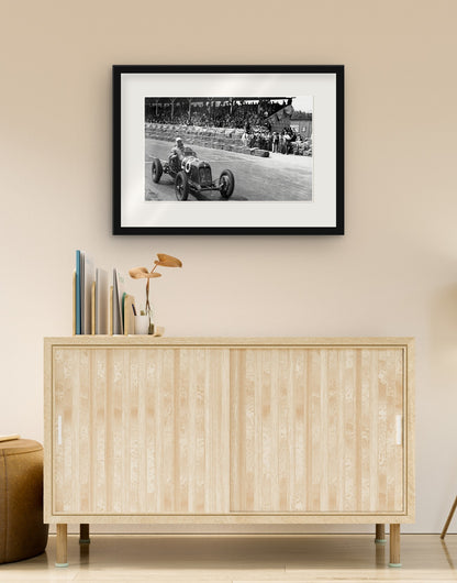 Stampa fine art di «Maserati sul circuito della Superba, Genova 1937» con cornice nera e passepartout, appesa in un soggiorno sopra una credenza